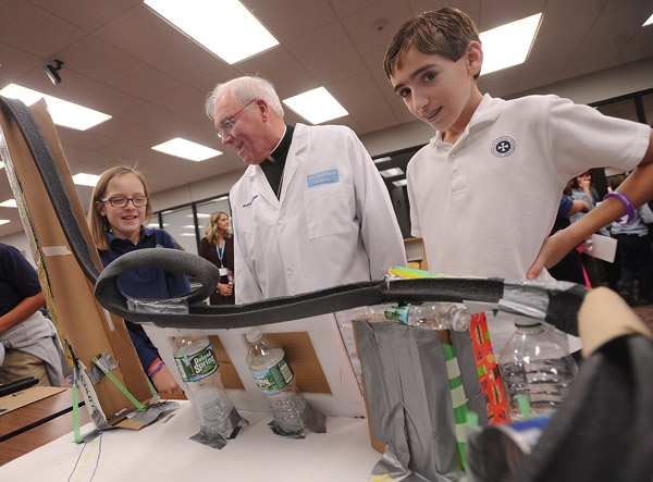 Bishop Richard Malone, wearing a lab coat presented to him by students, speaks with DeSales Catholic School sixth graders Riley Bell and Nico Scirri as they explain their 